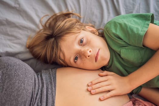 Young beautiful pregnant woman and eldest son. The cute boy leaned his ear against his mother's belly. Expecting a baby in the family concept. Preparing an older child for a younger one.