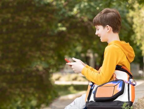 Happy caucasian boy using a smart phone on the street. Time after school