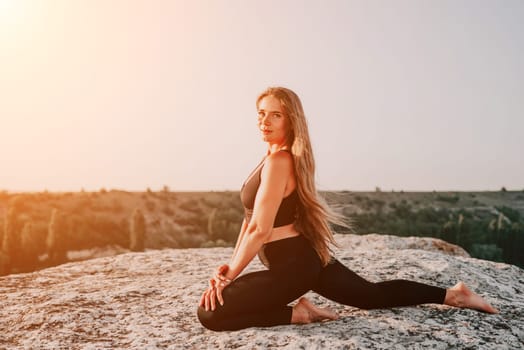 Well looking middle aged woman with long hair, fitness instructor in leggings and tops doing stretching and pilates on the rock near forest. Female fitness yoga routine concept. Healthy lifestyle.