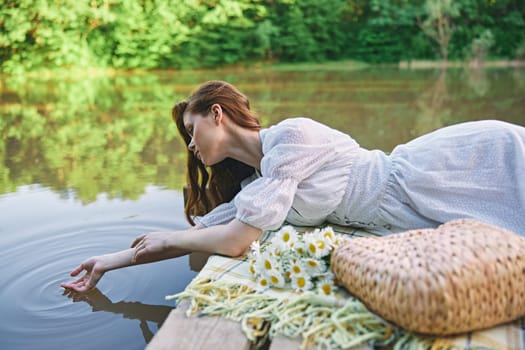 a sophisticated woman in a light dress touches the water while relaxing by the lake. High quality photo