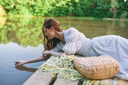 a sophisticated woman in a light dress touches the water while relaxing by the lake. High quality photo