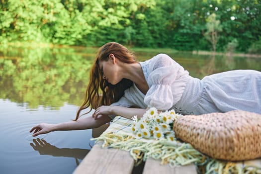 a sophisticated woman in a light dress touches the water while relaxing by the lake. High quality photo