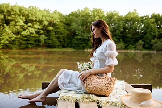 an elegant woman in a light dress sits on a pier by the lake with her feet in the water. High quality photo