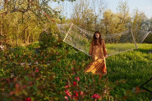 a happy woman in a long orange dress is resting in nature lying in a mesh hammock with her arms outstretched and looking at the sky. High quality photo