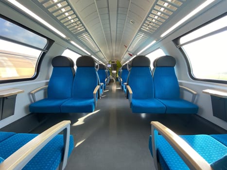 Empty cabin of a modern passenger train. Empty blue seats inside train cabin, corridor view, no people. Modern european economy class fast train interior.