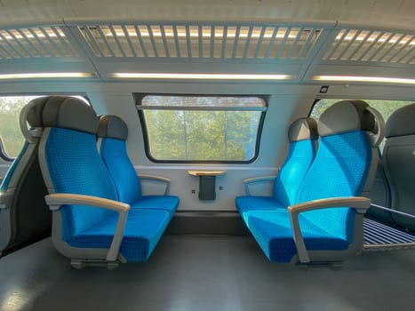 Empty cabin of a modern passenger train. Empty blue seats inside train cabin, corridor view, no people. Modern european economy class fast train interior.