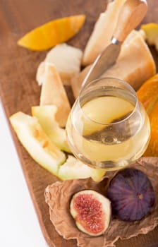 white wine, cheese, melon, grapes figs on a dark background