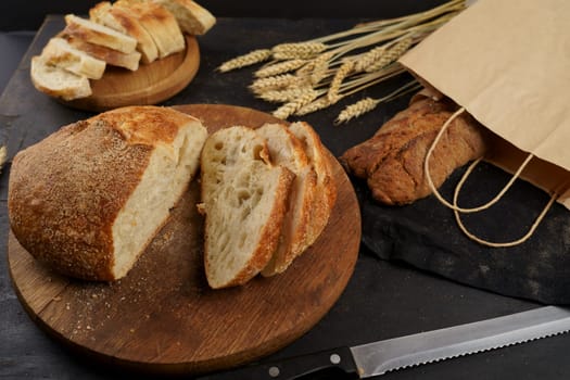 Concept of homemade bread, natural farm products, domestic production. Healthy and tasty organic food. Round loaf of freshly baked sourdough bread with knife on cutting board. Fresh bread slice and cutting knife on rustic table