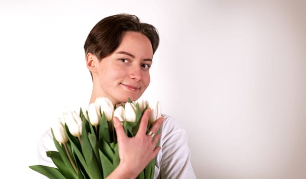 girl with brown eyes holding a bouquet of flowers, young beautiful cute model with tulips on a white background, smiling and looking at camera, front view.