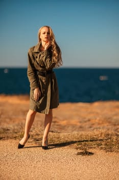 Portrait blonde sea cape. Calm young blonde in a khaki raincoat stands on the seashore.