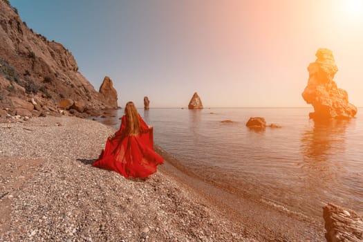 Beautiful sensual woman in a flying red dress and with long hair, stands on the seashore.