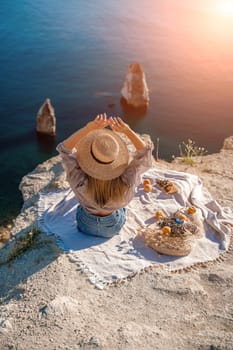 woman sea travel. photo of a beautiful woman with long blond hair in a pink shirt and denim shorts and a hat having a picnic on a hill overlooking the sea.