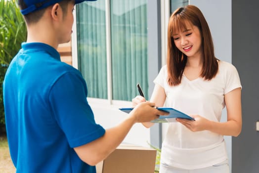 Asian beautiful customer young woman signing delivery in clipboard get her package from service courier man, smiling female signature receipt of delivery package at door front house