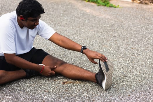 Close up Asian young athlete sport runner black man wear watch he sitting pull toe feet stretching legs and knee before running at outdoor street health park, healthy exercise before workout concept