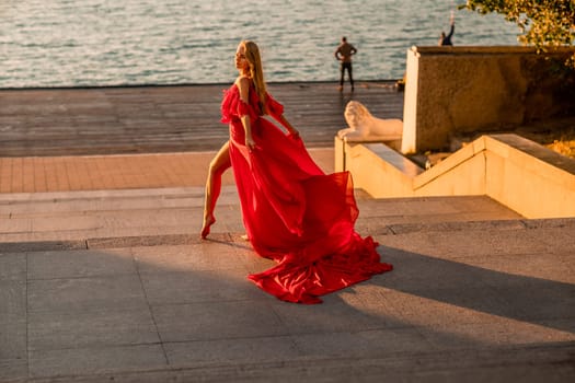 Sunrise red dress. A woman in a long red dress against the backdrop of sunrise, bright golden light of the sun's rays. The concept of femininity, harmony