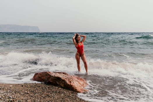 Woman travel sea. Young Happy woman in a long red dress posing on a beach near the sea on background of volcanic rocks, like in Iceland, sharing travel adventure journey