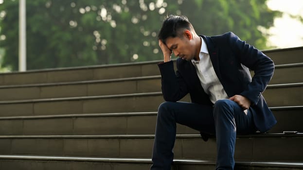 Image of upset man employee sitting on stairs outside office building, financial crisis, unemployed concept.