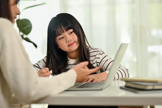 Interested Asian girl doing school assignment with tutor at home. Homeschooling and learning concept.