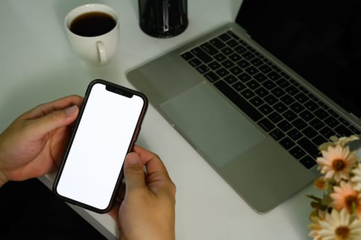 Closeup view of man sitting at office desk with laptop and using smartphone. Blank screen your advertising text message.