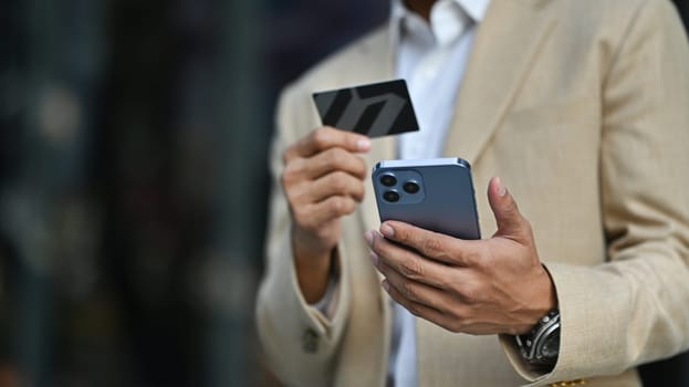 Modern businessman holds credit card and using smartphone. Banking, finance, online payment, e commerce.