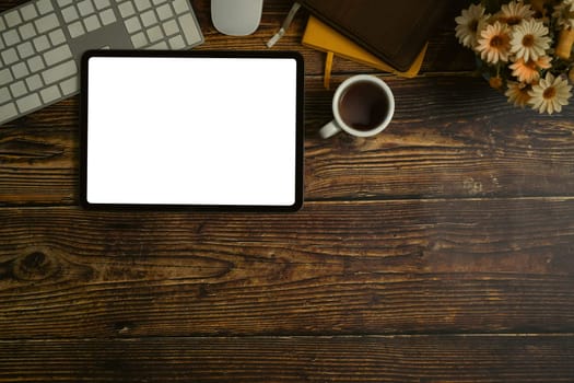 Top view of digital tablet with wireless keyboard, coffee cup and notebooks on wooden working desk.