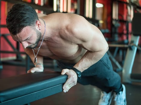 Attractive and fit young man in gym working out pecs and exercising on equipment, on a bench