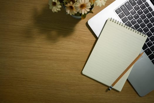 Blank spiral notepad, pencil and laptop computer in wooden working desk. Top view with copy space.