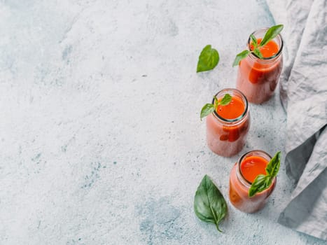 Delicious gaspacho soup in glass bottles. Traditional spanish cold soup puree gaspacho or gazpacho on gray cement background with copy space for text. View from above or top view or flat lay