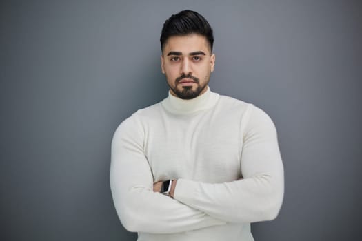 Portrait of a stylish man posing on a gray background with his arms crossed