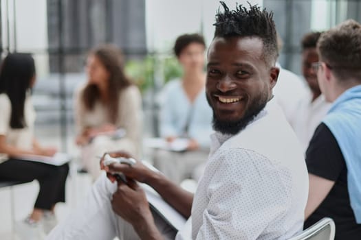 portrait of an African American in a white shirt against the background of his colleagues. looking at the camera