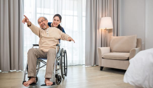 Asian senior retired old man sitting on wheelchair having fun with young woman nurse, Happy curator person doctor pushing and running elderly patient freedom raising arm, sanatorium