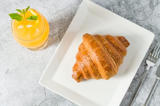 Croissant on a white porcelain plate with freshly squeezed orange juice on the side