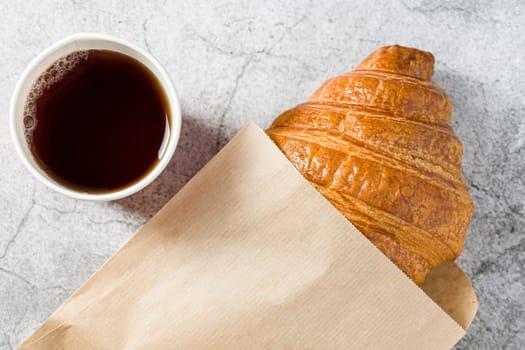 Fresh delicious croissant wrapped in paper with tea on the side