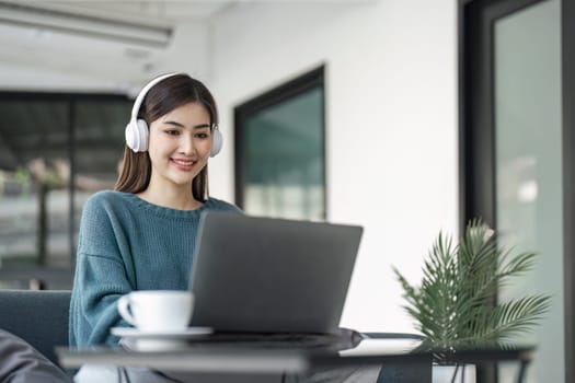 Young woman in modern headphones sit on couch in living room work on laptop.