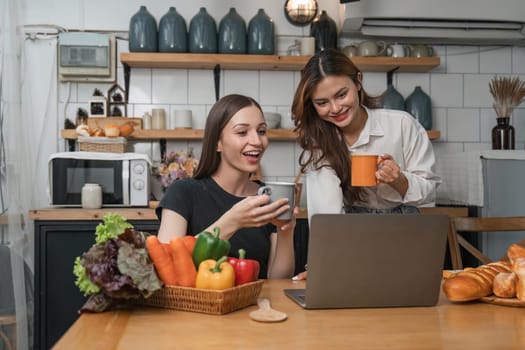 Two beautiful woman friends having breakfast and drinking coffee while talking in the kitchen at home.
