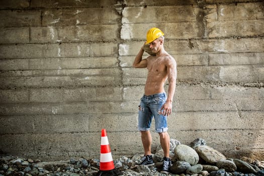 Sexy, muscular construction worker shirtless, working outdoor, wearing blue jeans and yellow hard-hat