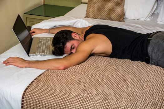 Close Up of Young Man with Dark Hair Sleeping on Bed Next to Laptop Computer and Cell Phone, Tired from Too Much Work