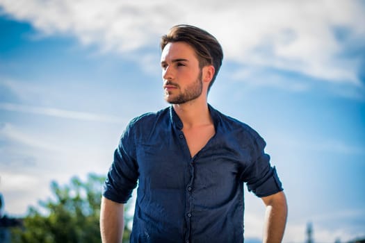 One handsome young man in urban setting in summer day, wearing blue shirt