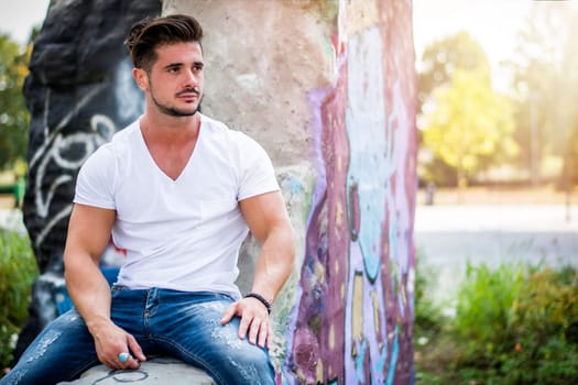 Handsome fit man in white t-shirt outdoor in city setting, looking away