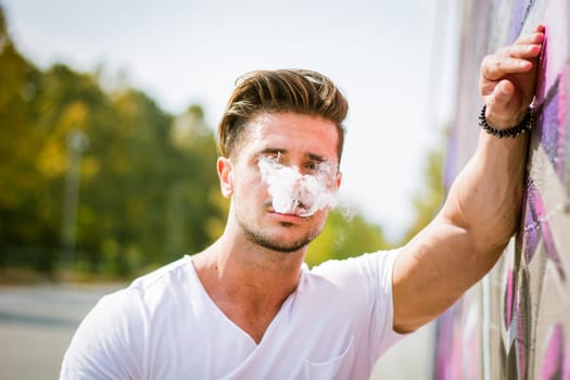 Handsome man smoking e-cigarette, vaping outdoor in city setting