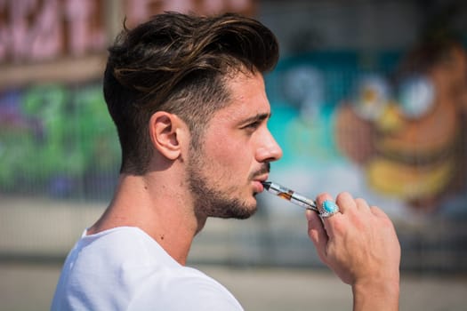 Handsome man smoking e-cigarette, vaping outdoor in city setting