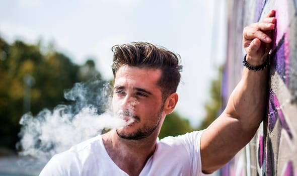 Handsome man smoking e-cigarette, vaping outdoor in city setting