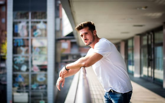 Handsome fit man in white t-shirt outdoor in city setting, looking away