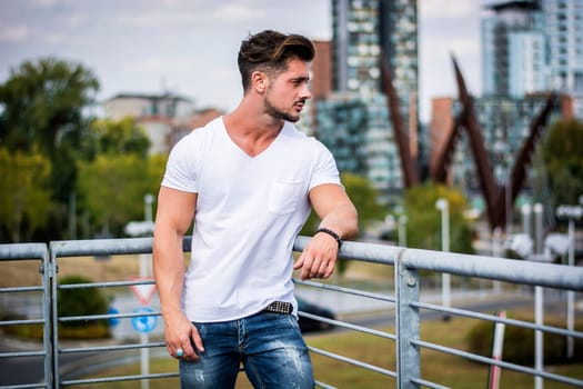 Handsome fit man in white t-shirt outdoor in city setting, looking away