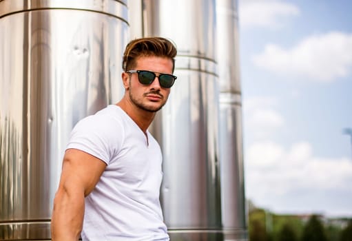 Handsome fit man in white t-shirt outdoor in city setting, looking at camera