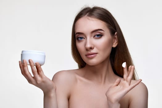 beautiful smiling young woman applying skin care cream on her face on white background