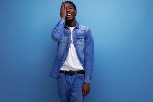 handsome american man with afro curls in casual denim outfit on blue background with copy space.