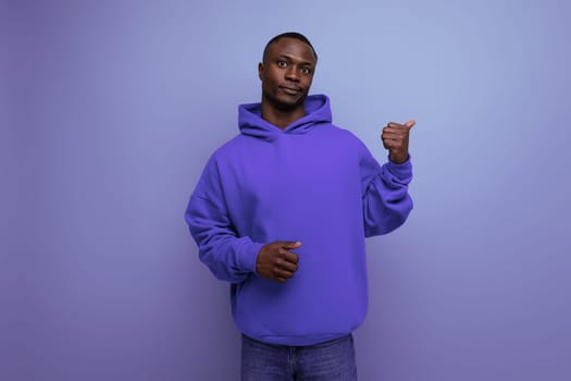 energetic positive young african man consultant in stylish hoodie shows with hand actual offer on studio background with copy space.