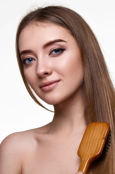 Beautiful smiling brunette woman looks at the camera and combs her hair with wooden brush isolated on white background