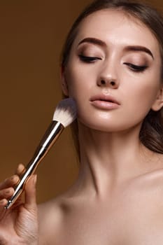 close-up, young woman applying blush on cheeks with make-up brush on beige background